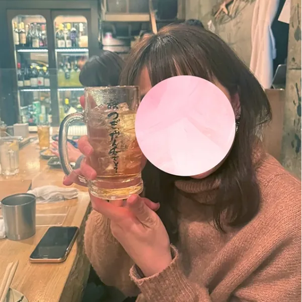 居酒屋のような場所でグラスを手に持ち、飲み物を楽しんでいる女性